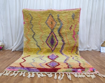 May include: A colorful Moroccan rug with a geometric pattern in shades of yellow, orange, red, purple, and pink. The rug has a fringe border and is made of wool.