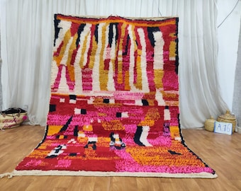 May include: A colorful Moroccan rug with a geometric pattern in shades of pink, red, orange, and white. The rug has a white fringe border.