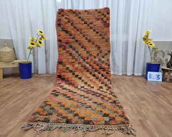 May include: A long, rectangular, orange, brown, and black Moroccan rug with a geometric pattern. The rug has fringe on the ends.