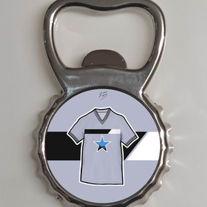 May include: A silver bottle opener with a round, blue, white, and black design featuring a stylized t-shirt with a star. The text "7 years FireH" is written in black on the design.