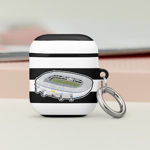 Könnte beinhalten: Schwarz-weiß gestreiftes Airpods-Case mit einem weißen Umriss eines Stadions, das auf der Vorderseite aufgedruckt ist. Das Case hat einen silbernen Metallring.