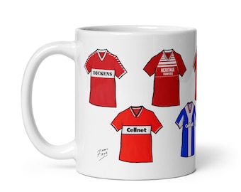 May include: White ceramic mug with a design of five different red and white soccer jerseys. The jerseys have different sponsors including Dickens, Heritage Hampers, and Cellnet. The mug is signed by 'Zuma Firth'.