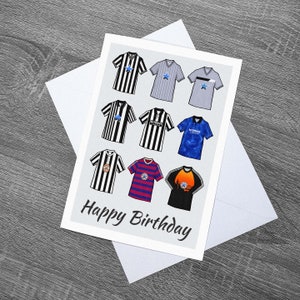 May include: A birthday card with a gray background featuring a collage of nine different soccer jerseys. The jerseys are in various colors and designs, including black and white stripes, blue and white stripes, and a blue jersey with a star. The text "Happy Birthday" is printed in black at the bottom of the card.