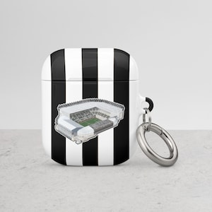 Puede incluir: Funda para Airpods a rayas blancas y negras con una imagen en blanco y negro de un estadio en la parte delantera. La funda tiene un anillo plateado.