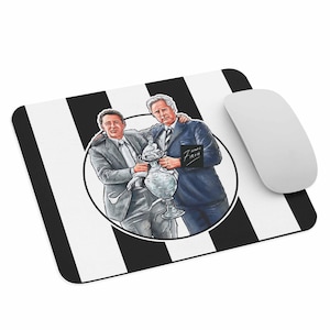 May include: Mousepad with a black and white striped background. The mousepad features a circular illustration of two men holding a trophy. The illustration is surrounded by a black circle. A white computer mouse is on the right side of the mousepad.