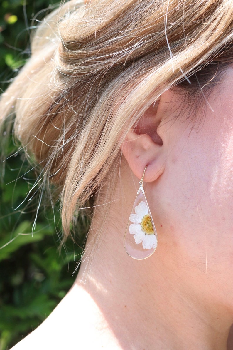 May include: A pair of teardrop-shaped earrings with a white flower pressed inside each clear resin drop.