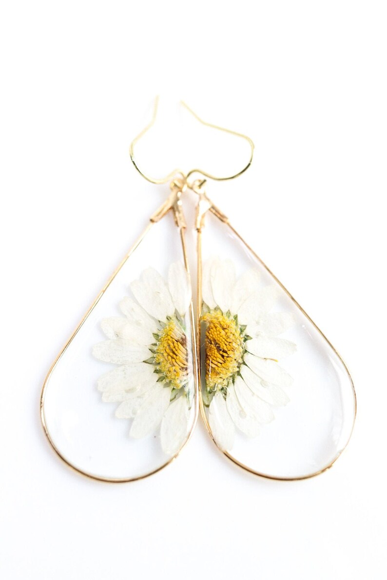 May include: Gold teardrop earrings with a pressed white daisy flower inside each earring.