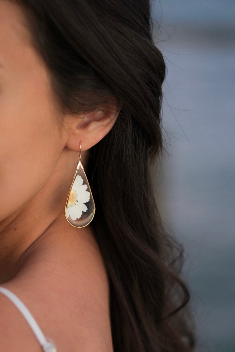 May include: Gold teardrop earrings with a pressed white flower inside the teardrop.
