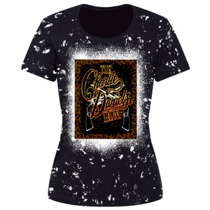 May include: Black t-shirt with a white splatter pattern. The front of the shirt features a graphic of a leopard print square with the text "THE Charlie Daniels BAND" in a gold and orange gradient.