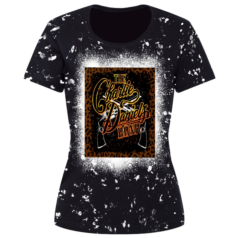 May include: Black t-shirt with a white splatter pattern. The front of the shirt features a graphic of a leopard print square with the text "THE Charlie Daniels BAND" in a gold and orange gradient.