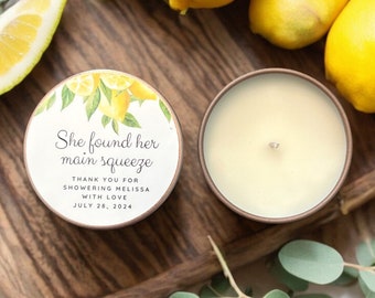 May include: A round candle with a white label that says "She found her main squeeze" with a lemon illustration. The label also includes the text "Thank you for showering Melissa with love July 28, 2024".
