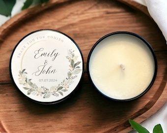 May include: A white candle with a black lid on a wooden tray. The candle has a label that says "Thank you for coming Emily & John 07.07.2024" with a floral design.