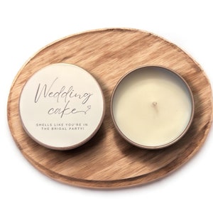 May include: A white candle tin with the text "Wedding cake" and "Smells like you're in the bridal party!" on a wooden tray.