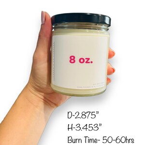 May include: A clear glass candle jar with a black lid. The jar is labeled "8 oz." and has a pink font. The candle is hand-poured and has a burn time of 50-60 hours. The jar is 2.875 inches in diameter and 3.453 inches in height.