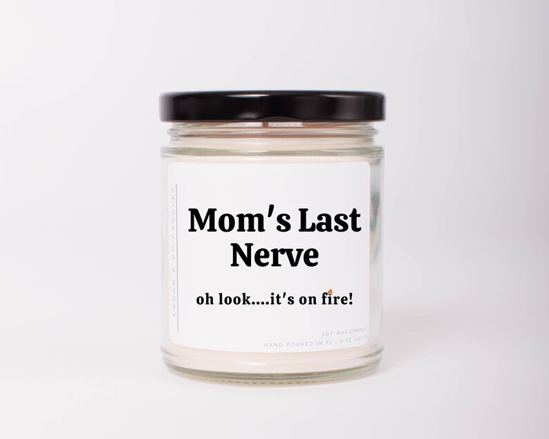 May include: A white candle jar with a black lid. The label reads "Mom's Last Nerve" and "oh look....it's on fire!"