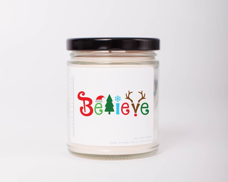 K&ouml;nnte beinhalten: Ein klares Glas-Kerzenglas mit schwarzem Deckel. Das Etikett zeigt das Wort "Believe" in farbenfrohen, festlichen Buchstaben mit weihnachtlichen Symbolen. Die Kerze ist handgegossen und enth&auml;lt 227g Sojawachs.