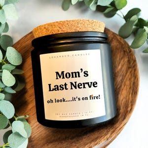 May include: Black soy wax candle with a cork lid. The label reads "Mom's Last Nerve oh look....it's on fire!" and "LOGAN & CO. CANDLES". The candle is 12 oz and hand-poured in Florida.