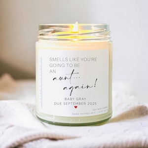 May include: A white candle with a black label that reads "Smells like you're going to be an aunt... again! Baby Gray Due September 2025".