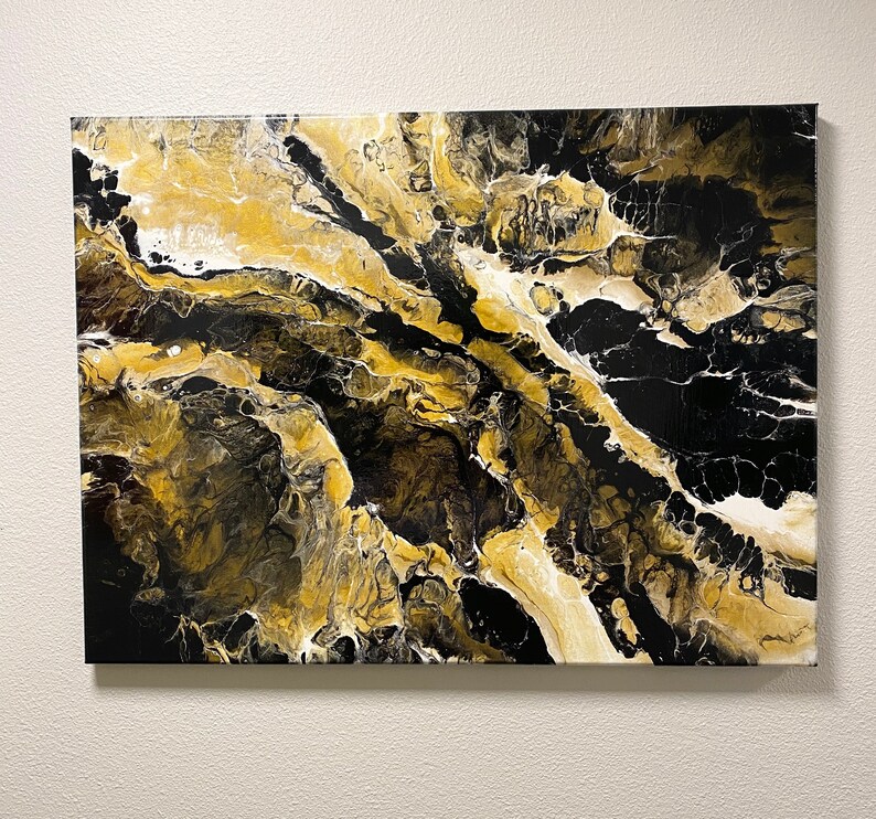 May include: Abstract art canvas with a fluid design. The artwork features a blend of black, gold, and white acrylic paints. The colors are swirled and layered to create a marbled effect, with a glossy finish. The canvas is rectangular and mounted on a wooden frame.