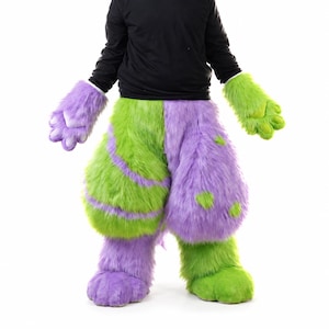 May include: A plush costume featuring a black long-sleeve shirt, purple and lime green faux fur pants with a spotted pattern, and matching oversized furry hand paws. The left paw is purple with white accents, and the right paw is lime green.