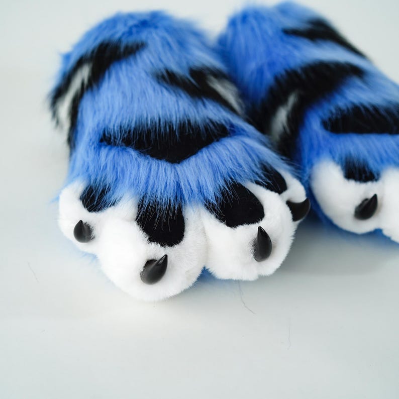 May include: A pair of blue and black faux fur paws with white paw pads and black claws. The furry paws have a realistic design, perfect for cosplay or costume use.