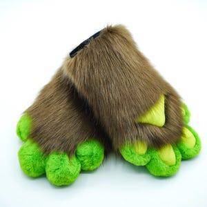 May include: A pair of brown furry slippers with green claws. The slippers are made of soft, plush fabric and have a realistic paw design.