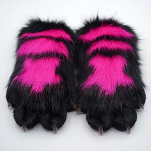 May include: A pair of black and pink furry paw-shaped hand warmers with black claws.