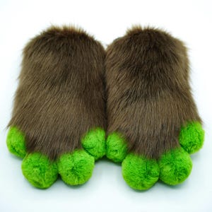 May include: A pair of brown furry slippers with green paw-shaped toes. The slippers are soft and plush, perfect for keeping your feet warm.