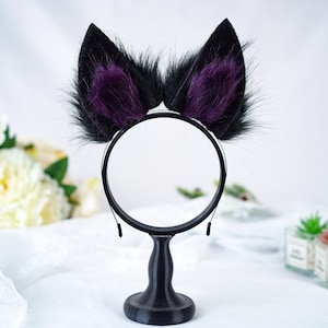 May include: Black cat ears headband with purple fur tips. The headband is on a black stand.