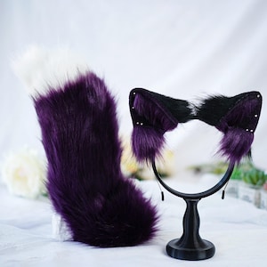 Peut inclure: Queue de chat et serre-tête en fausse fourrure violette et blanche avec des oreilles noires. Le serre-tête a un élastique noir et la queue a une pointe blanche.