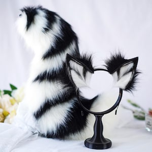 May include: Black and white striped fluffy tail and matching cat ears headband. The tail is long and fluffy, and the ears are soft and plush. The headband is black with white fur on the ears.