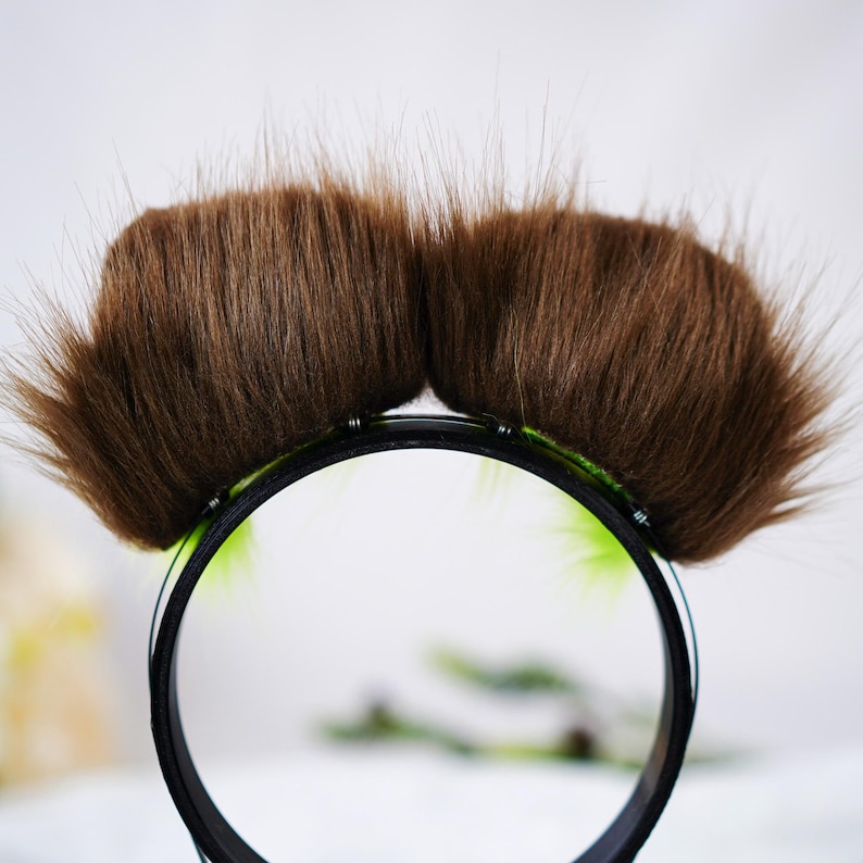 Puede incluir: Una diadema negra con dos mechones de pelo sint&eacute;tico marr&oacute;n, dise&ntilde;ados para parecer un bigote. La diadema tiene un ribete verde. Este accesorio es probablemente para disfraces o fines de novedad.