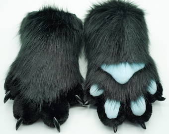 Puede incluir: Un par de patas peludas negras con almohadillas azules y garras negras. Las patas están hechas de tela de felpa suave y están diseñadas para parecer patas de animales.