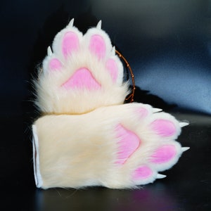 May include: A pair of white furry paws with pink paw pads. The paws are attached to a white furry wrist cuff.
