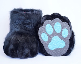 Puede incluir: Zapatillas negras con forma de pata y peludas. Las zapatillas tienen un aspecto afelpado y texturizado. Las suelas son grises con huellas de patas de color azul claro. Las zapatillas están diseñadas para parecerse a patas de animales.