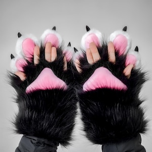 May include: A pair of black faux fur paw gloves with pink paw pads and white accents. The gloves have black claws at the tips of the fingers. The gloves are designed to resemble animal paws.