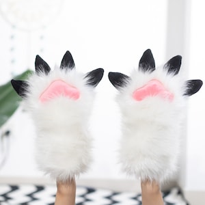May include: A pair of white fuzzy cat paw hand warmers with black claws and pink paw pads.