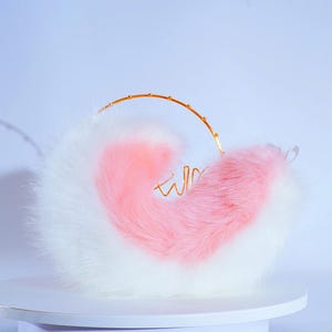 May include: A fluffy white and pink tail with a gold wire hoop. The tail is curled into a heart shape.