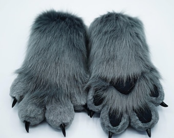 Puede incluir: Un par de pantuflas de piel gris con dedos en forma de pata. Las pantuflas tienen una textura suave y mullida y son perfectas para mantener los pies calientes.