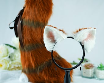 May include: A white faux fur cat ear headband with a black headband. The headband is on a stand in front of a fluffy red and brown tail.
