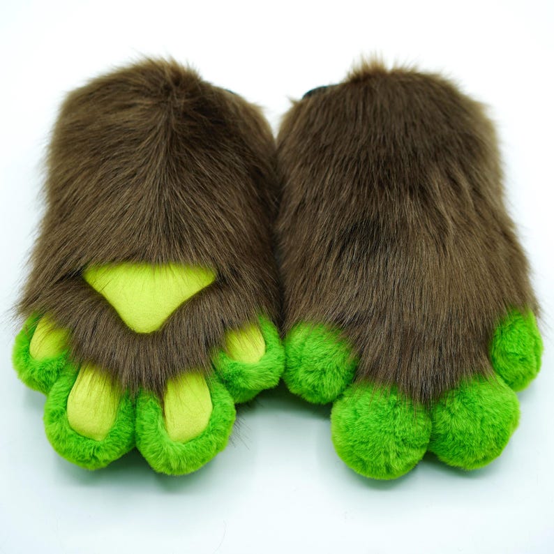 May include: A pair of brown furry slippers with green paw pads. The slippers have a realistic paw design with four toes on each foot.