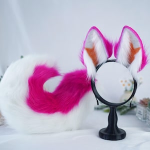 May include: A white and pink fluffy tail with a headband featuring two pink and white furry ears with orange accents. The headband is on a black stand.