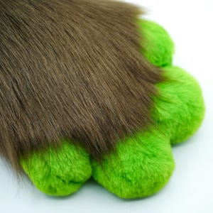May include: A brown furry tail with green paw pads. The tail is soft and fluffy, and the paw pads are made of a plush material.