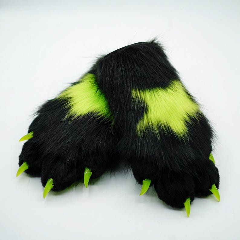 Puede incluir: Un par de patas peludas negras con garras verdes y detalles en verde ne&oacute;n. Las patas est&aacute;n dise&ntilde;adas para parecer patas de animales.