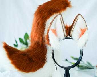 May include: A brown and white faux fur tail with a matching headband featuring white ears with orange tips. The tail is curled and the headband is on a black stand.