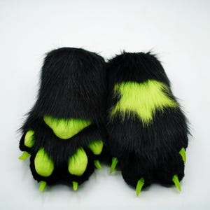 Puede incluir: Un par de patas peludas negras con garras verdes y detalles verdes. Las patas est&aacute;n dise&ntilde;adas para parecer patas de animales.