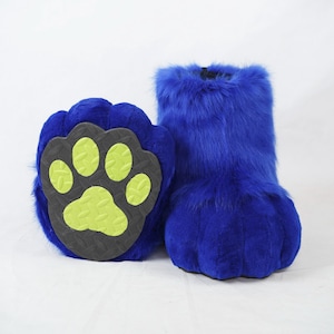 May include: A pair of blue furry paw-shaped slippers with a green paw print on the bottom of one slipper.