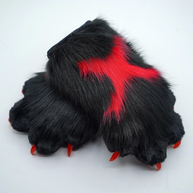 May include: Black furry paw with red accents. The paw has claws and is made of plush fabric.
