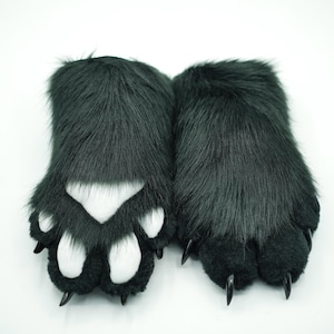 May include: A pair of plush black furry paws with white paw pads and black claws. The paws are designed to look like animal paws.
