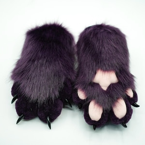 May include: A pair of plush purple paw hand warmers with black claws. The paw pads are a light pink color.